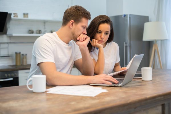 Man and woman looking over paperwork with computer and mugs