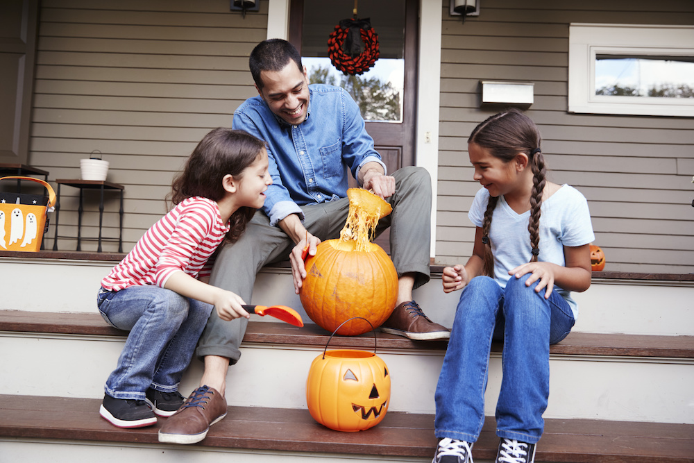 Father And Daughters Carving Halloween Pumpkin On House Steps