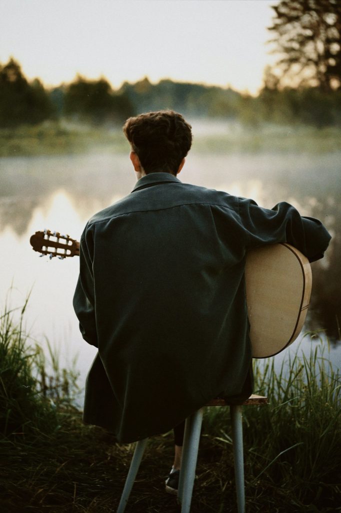 back shot of a man playing guitar by the lake