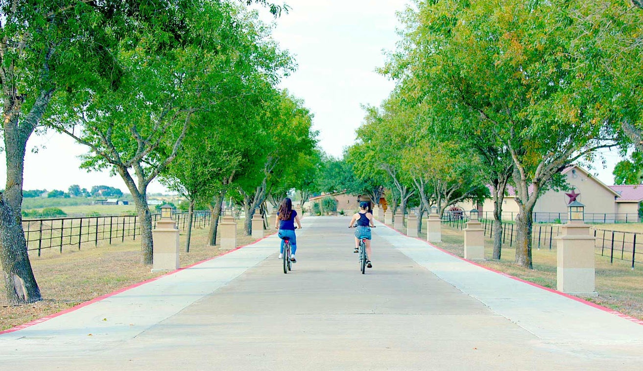 Two residents biking down the tree-lined ranch road