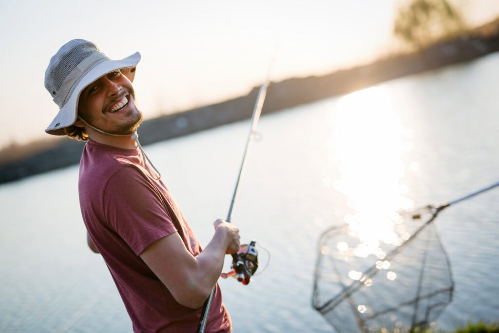 Man smiling while fishing at sunset by a lake