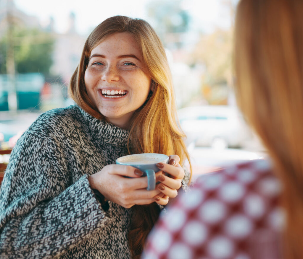 Smiling woman enjoying coffee with a friend outdoors